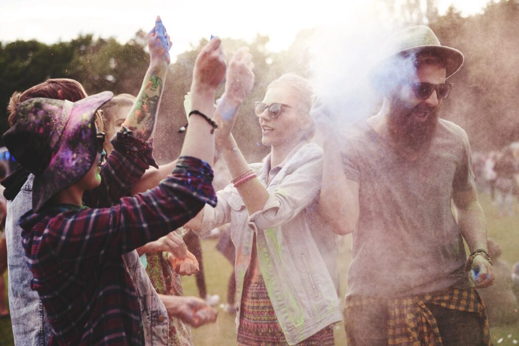 A group of people outdoors in Winter Haven, Florida, throwing colorful powder in the air and celebrating with smiles, with trees visible in the background.